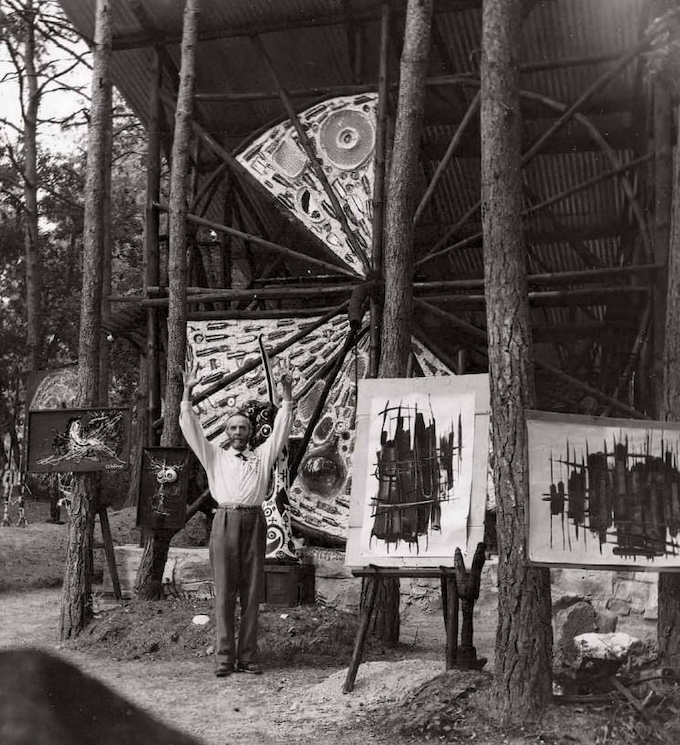 Chomo entre ses peintures et ses sculptures, devant l’Église des pauvres en construction, c. 1965